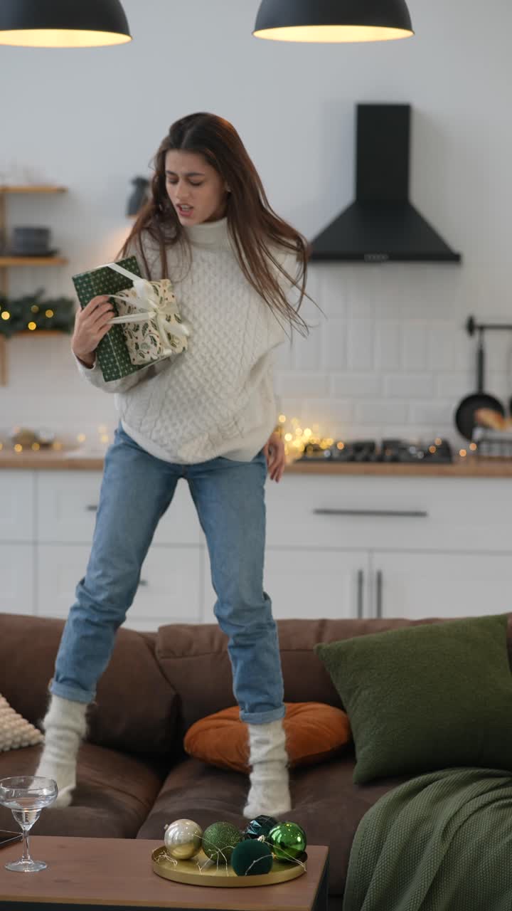 девушка с волнением прыгает на диване с рождественским подарком.