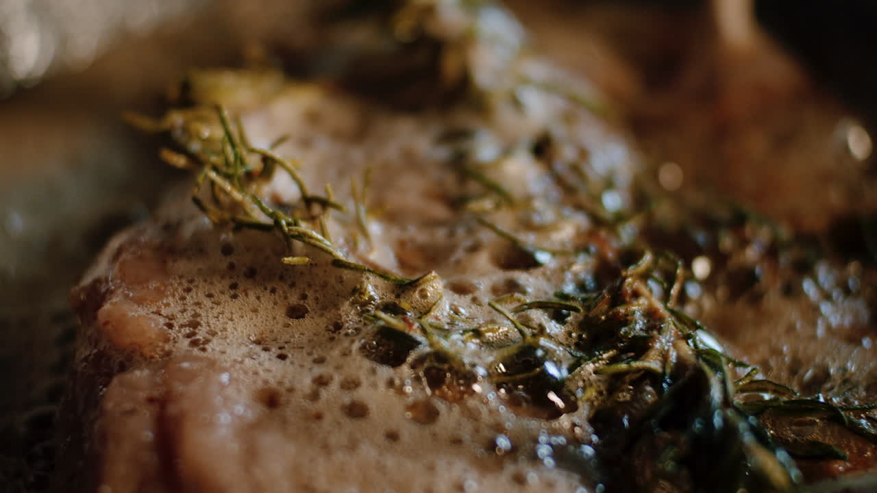 Spoon melted butter over meat in pan with rosemary, close up