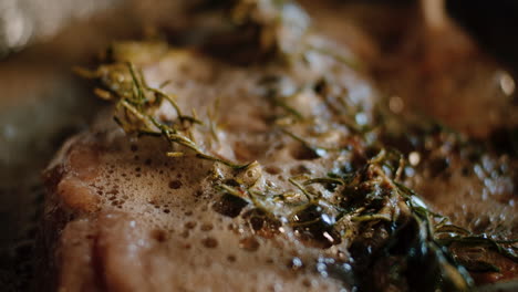 spoon melted butter over meat in pan with rosemary, close up