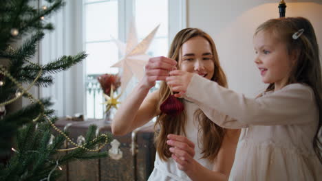 Adorable-mom-daughter-decorating-Christmas-tree-closeup.-Woman-giving-toy-baby