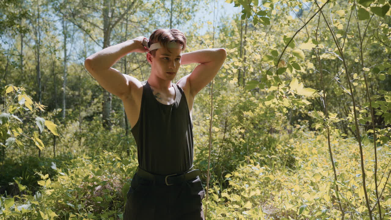 Front view of warrior standing in dense forest surrounded by green leaves and branches, tying white headband around forehead, sweat glistening on skin under dappled sunlight illuminating scene