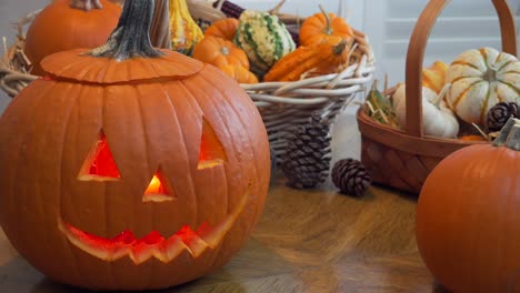 Dolly-En-Tiro-De-Jack-o-lantern-Iluminado-Con-Una-Vela-Sentada-En-Una-Mesa-De-Comedor-Luz-Natural-Desde-El-Lado-Con-Cesta-De-Calabaza-Ornamental