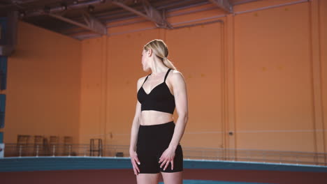 blonde sportvrouw aan het opwarmen en haar nek strekken in een indoor sportfaciliteit