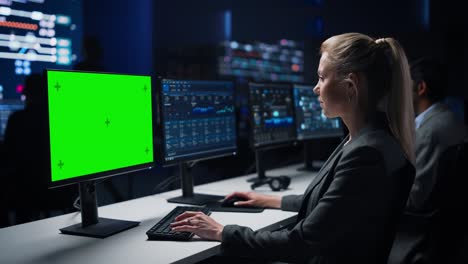 confident female data scientist works on green chroma key screen computer in big infrastructure control room. specialists use computers showing graphs, information. control room professional team