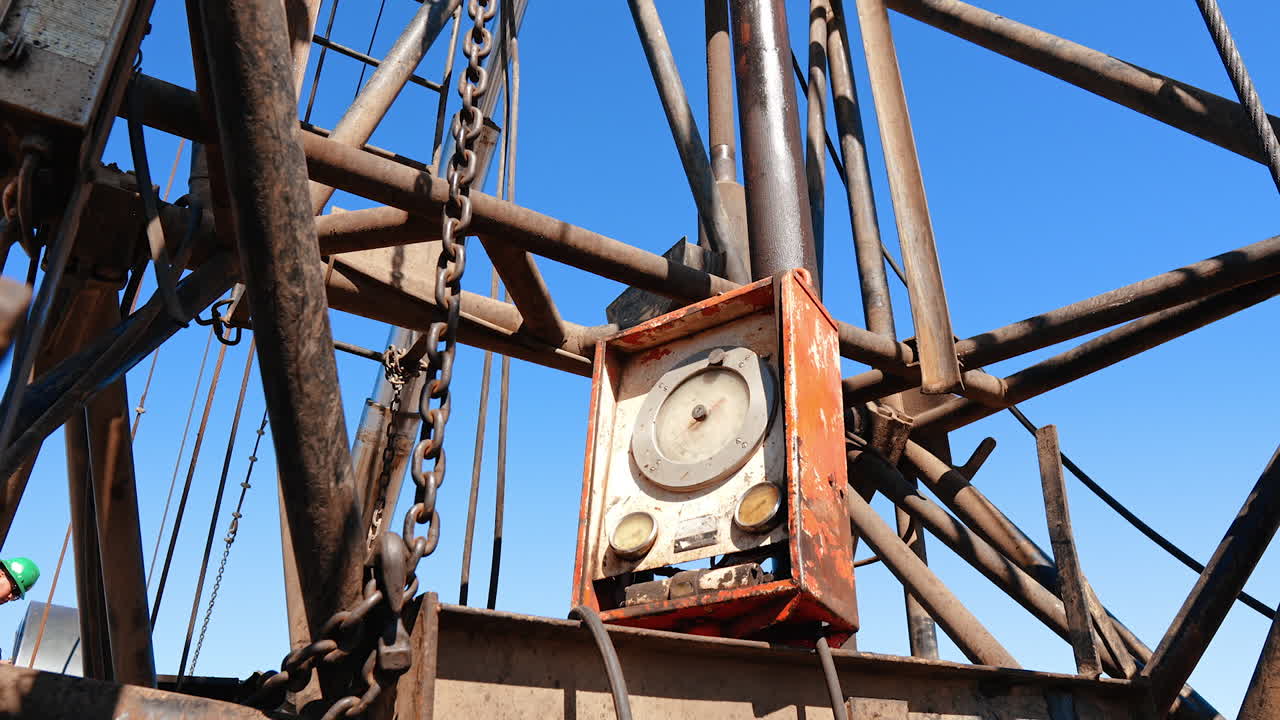 Pipes, chains and control desk at the drilling site. Equipment for natural resources production. Low angle view.