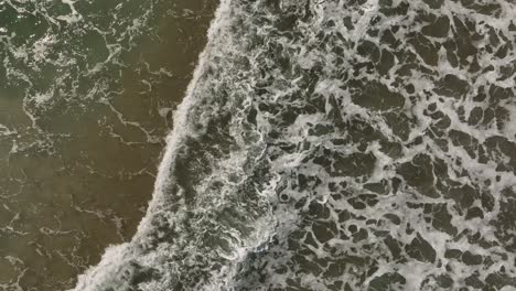 waves breaking along shoreline of beach top down aerial