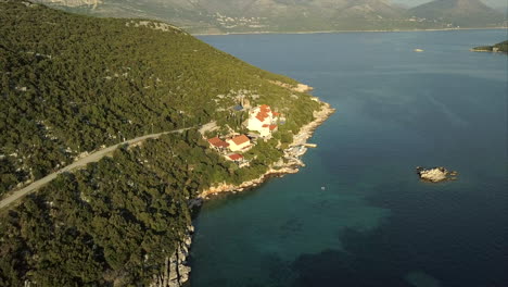 seguimiento de video aéreo a lo largo de la costa de una pequeña isla con colinas montañosas continentales, en la distancia