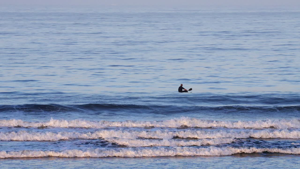 부서지는 파도를 헤치고 노를 저은 후 휴식을 취하는 카약의 남자 - 캘리포니아 라이프스타일