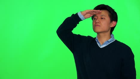 a young asian man looks for someone while protecting his eyes against the sun with his hand - green screen studio