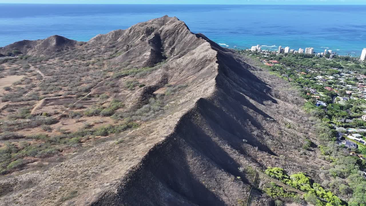 Aerial drone footage along the rim of Diamond Head volcanic crater on Oahu, Hawaii, showcasing panoramic tropical landscapes, turquoise ocean views, palm trees, and the scenic Waikiki coastline below