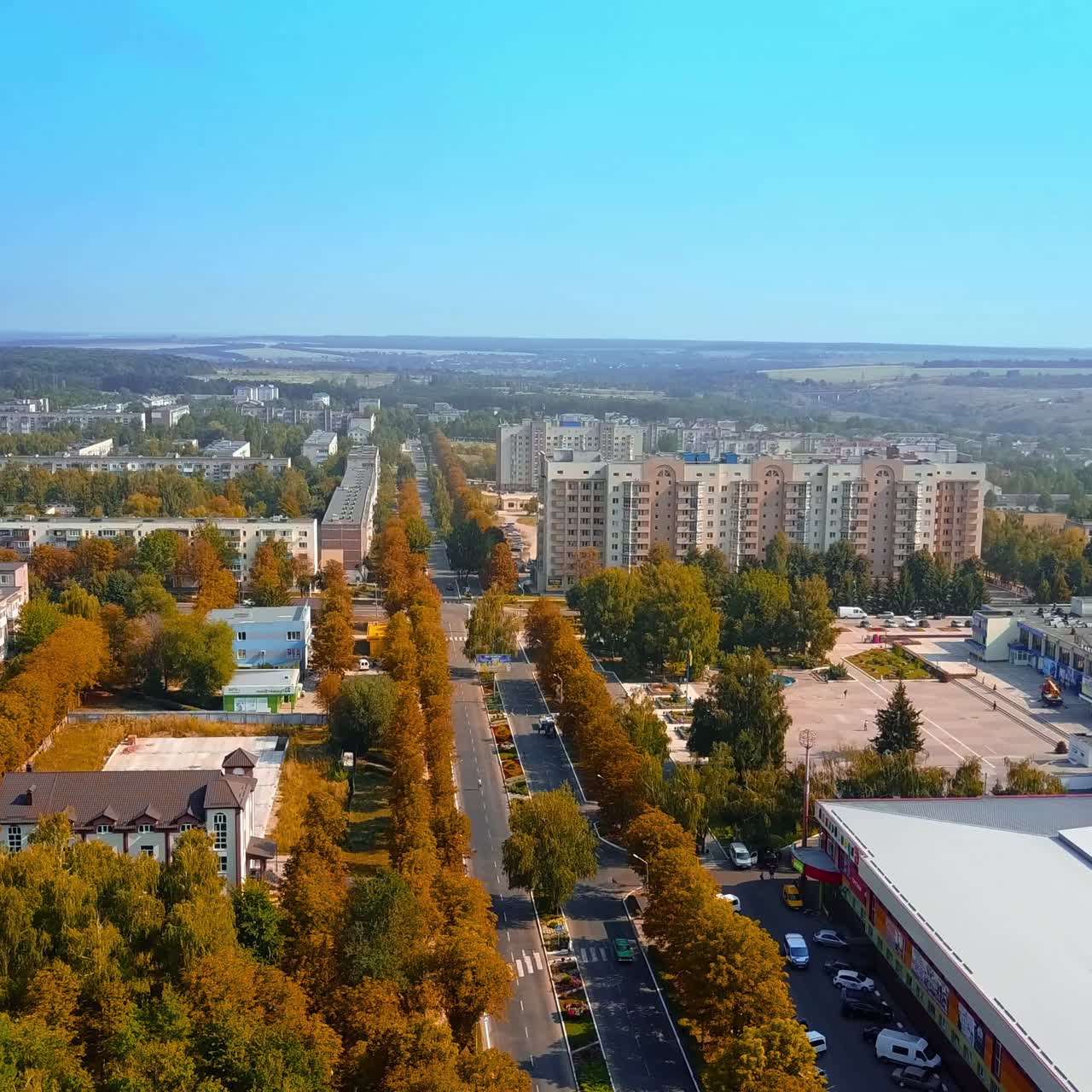 Flying along the road through the provincial city. Aerial view over the multi-storied buildings on sunny day
