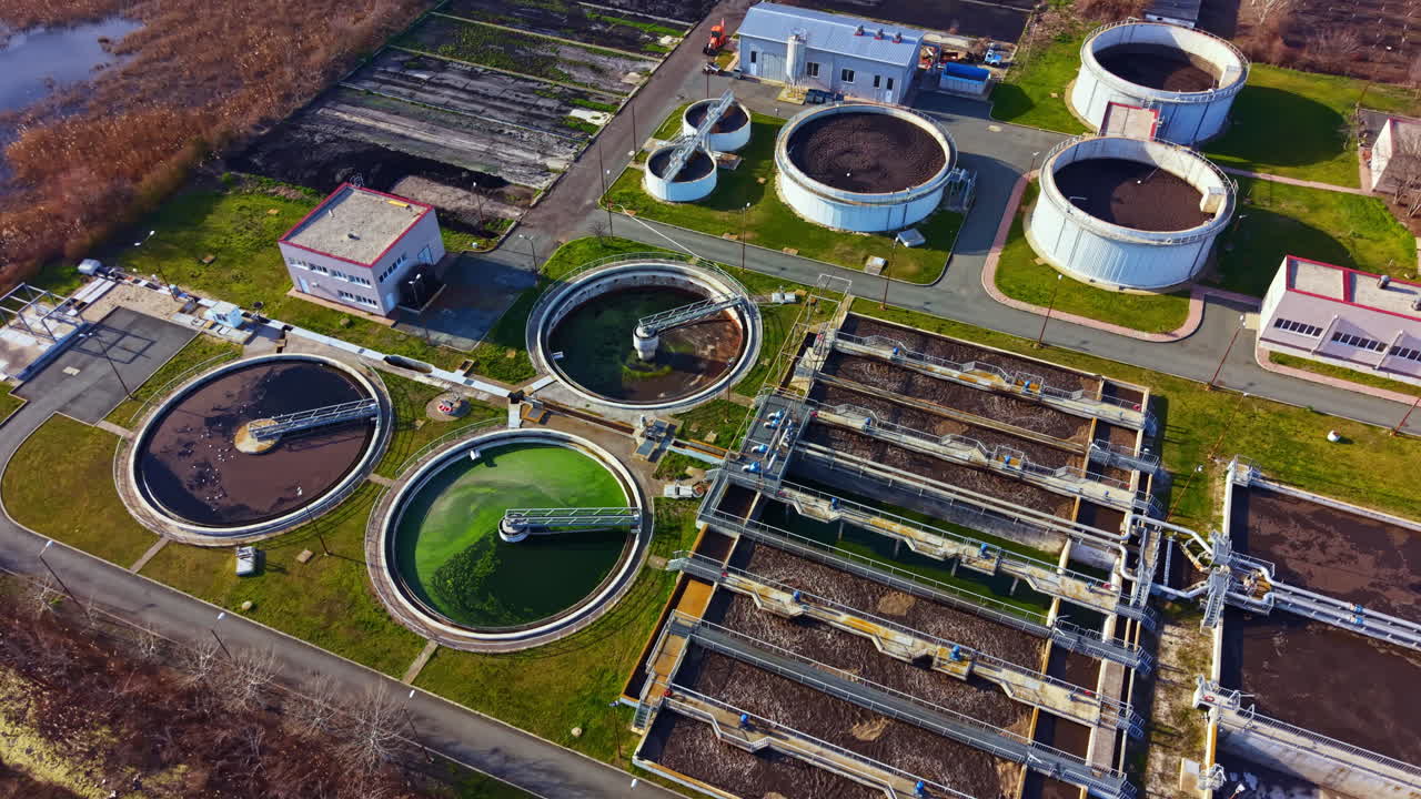 Water treatment facility located in an industrial area processes wastewater using large circular and rectangular tanks during a clear day