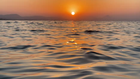 view from a kayak. beautiful warm sunset on denia beach, valencia spain. red sun reflects in a calm sea with small waves.