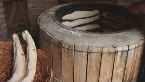 Mujer-Panadera-Sacando-El-Pan-Shoti-Recién-Horneado-De-Una-Estufa-De-Arcilla-Redonda-Usando-Un-Palo-De-Hierro