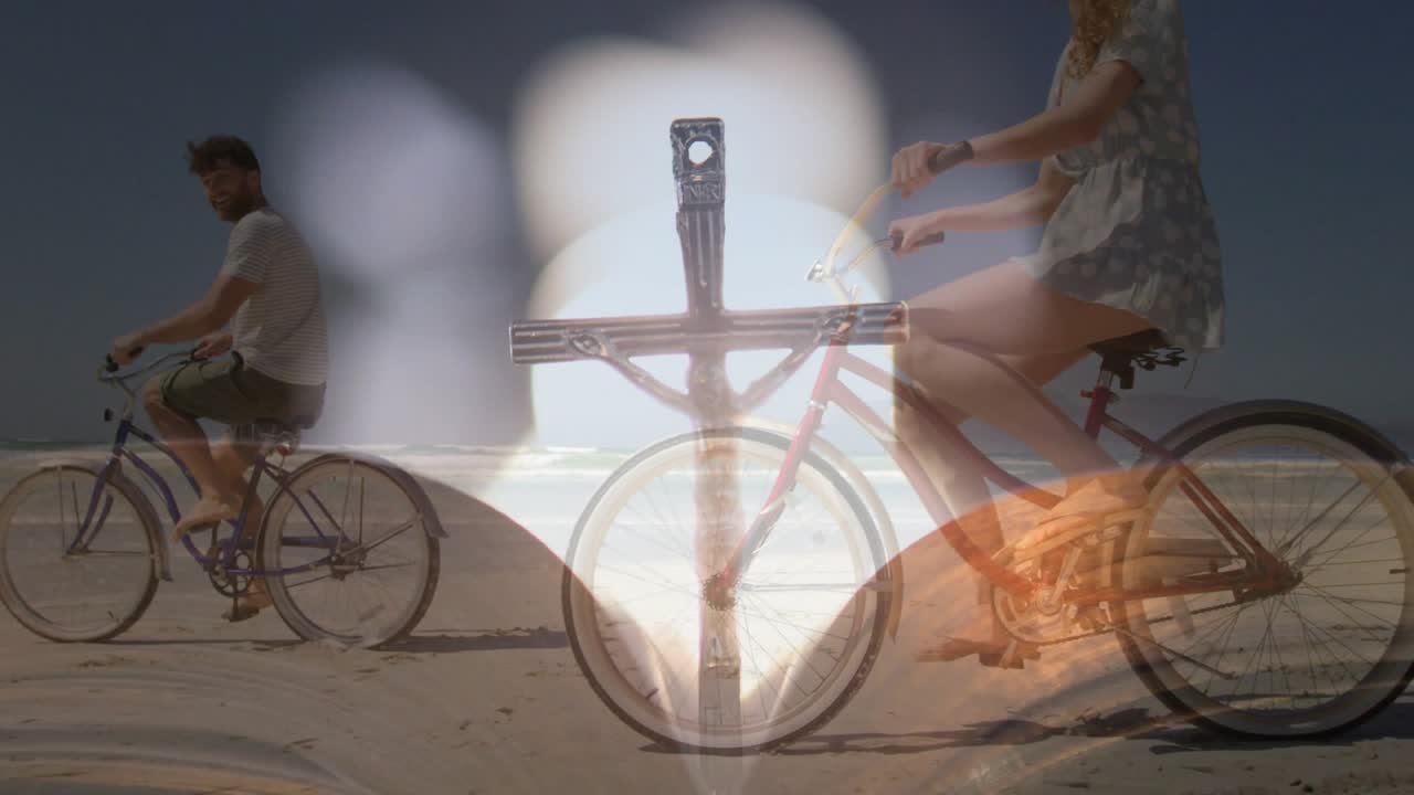 Couple bicycling shoreline, bottom center flare growing into metal cross bokeh for leisure travel