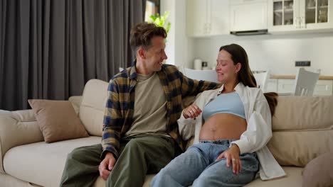 Happy-middle-aged-man-in-a-plaid-shirt-sits-on-the-sofa-with-his-pregnant-wife-and-talks-about-the-unborn-child-at-home