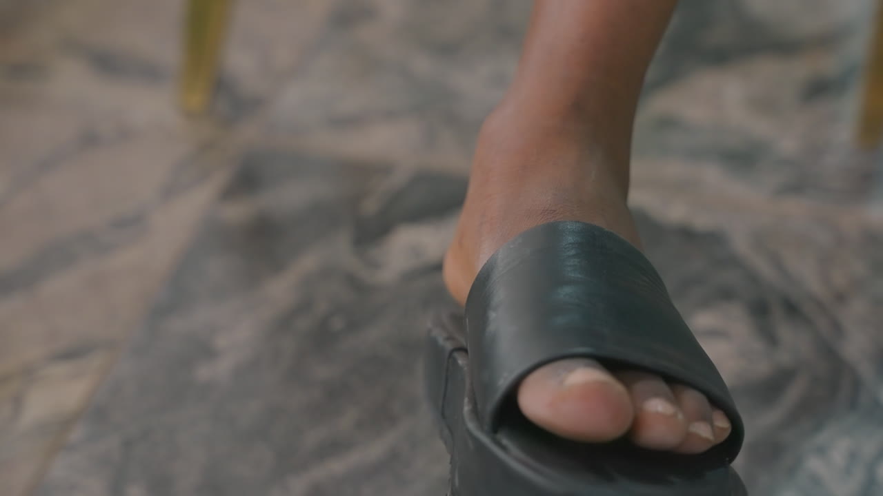 Nærbillede af fod i lædersandal, person slapper af under intim hjemmedate, blødt tæppe under fødderne, diskret tåbevægelse, varme dæmpede toner og ægte hjemlig stemning til romantisk fortælling