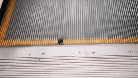 black object rotates on moving escalator as it goes up, yellow markings on sides of the escalator wall are visible, with the place up, emphasizing the mechanical and motion aspect of the scene