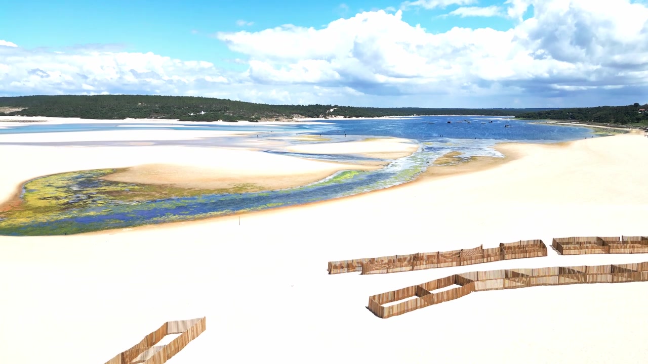 Luftfoto af sandstrand, lagune og sandfang under en klar daghimmel.