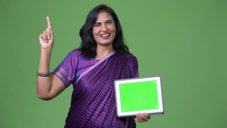 mature happy beautiful indian woman showing digital tablet and pointing finger up