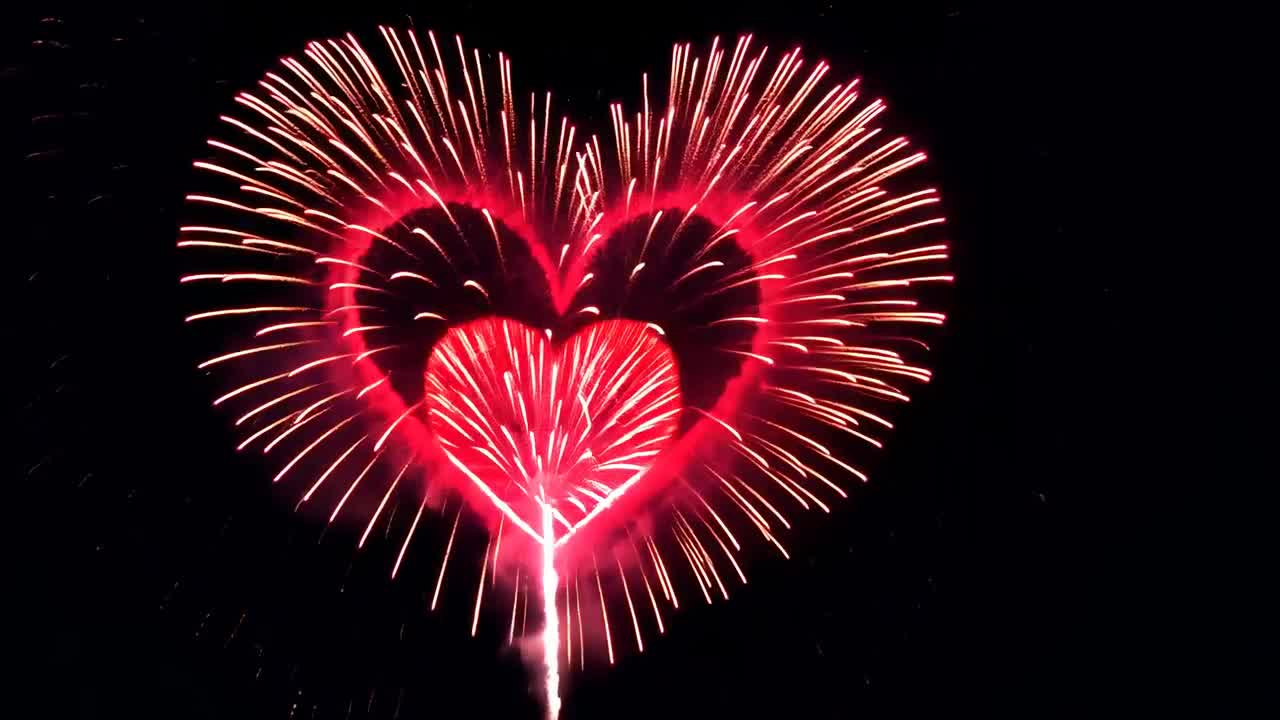 Aerial view of heart-shaped fireworks bursting in the night sky, captured in a vibrant, celebratory