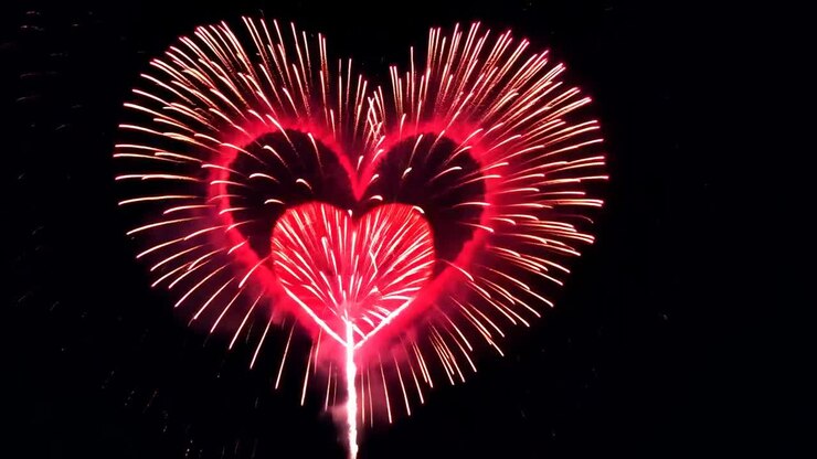 Aerial view of heart-shaped fireworks bursting in the night sky, captured in a vibrant, celebratory