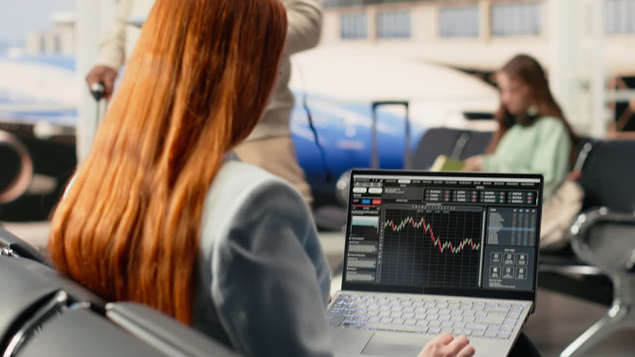 Kvinde analyserer finansielle diagrammer på bærbar computer i lufthavnens venteområde