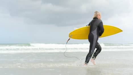 Side-view-of-old-caucasian-senior-woman-running-with-surfboard-at-beach-4k