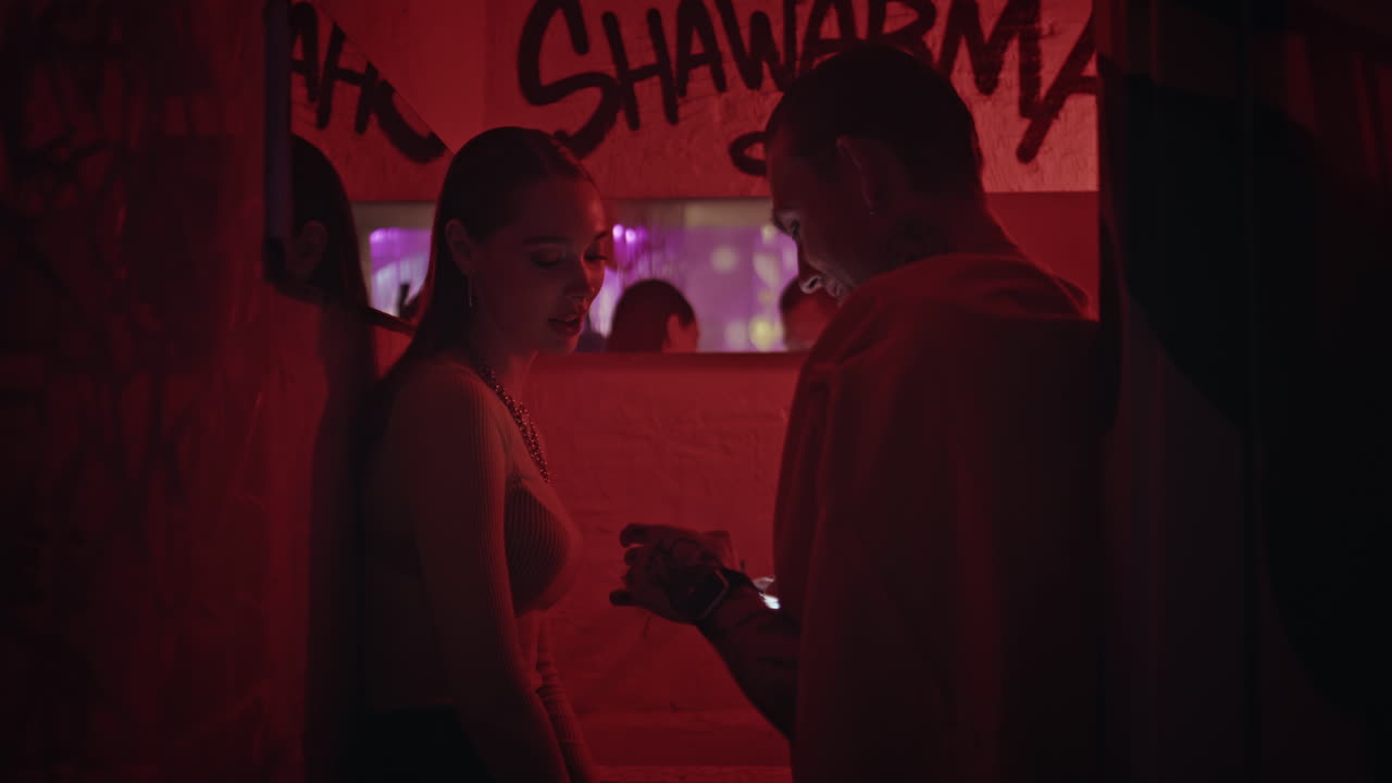 Intimate pair talking together in club hallway illuminated by red neon light