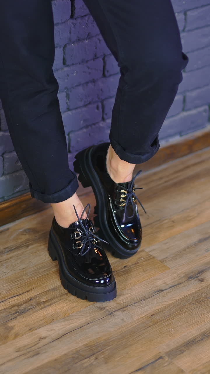Woman wearing black massive shoes with laces and tractor soles. Lady stands leaned on the blue wall demonstrating fashionable footwear. Vertical video
