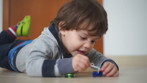 Un-Niño-Pequeño-Tirado-En-El-Suelo,-Jugando-Con-Sus-Juguetes-De-Cerca