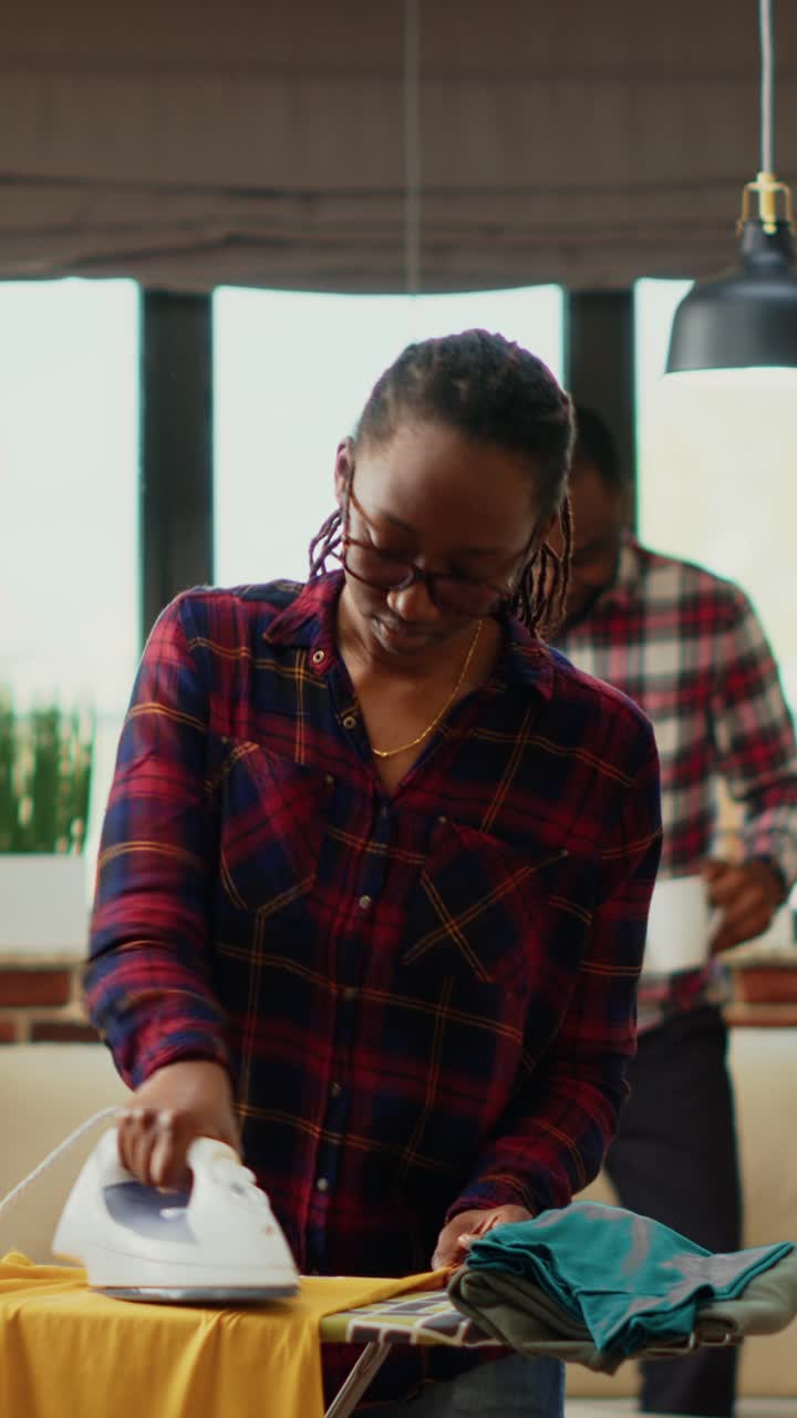 Vertical video: African american adult using steam on ironing table to do spring cleaning