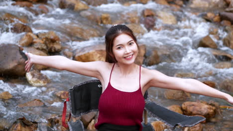 asian woman in red sitting on a chair with big rocks and water slow splashing for relaxing and happiness in the vacation summertime