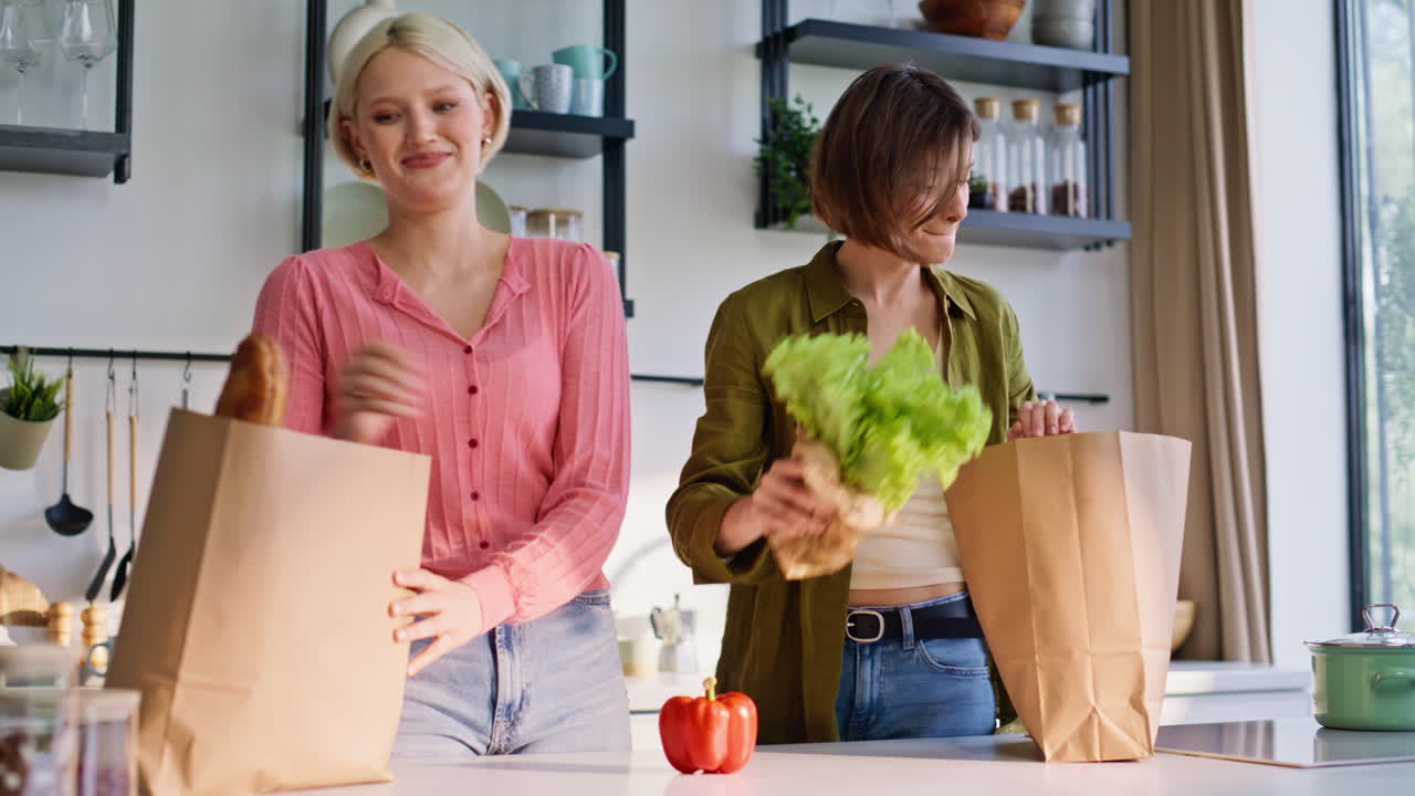 Primer plano de manos de mujer que llevan la compra. Dos chicas llegan a la tienda y colocan las compras.