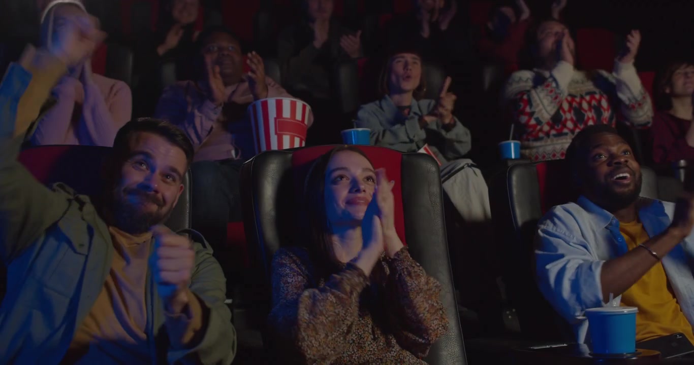 Grupo diverso de amigos aplaudindo numa sala de cinema.
