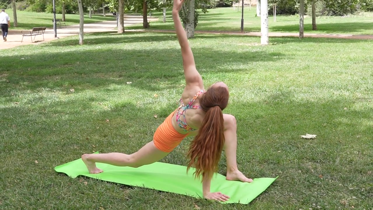 Eine Frau macht Yoga im Freien auf einer grünen Matte, übt Posen und genießt die ruhige Atmosphäre.