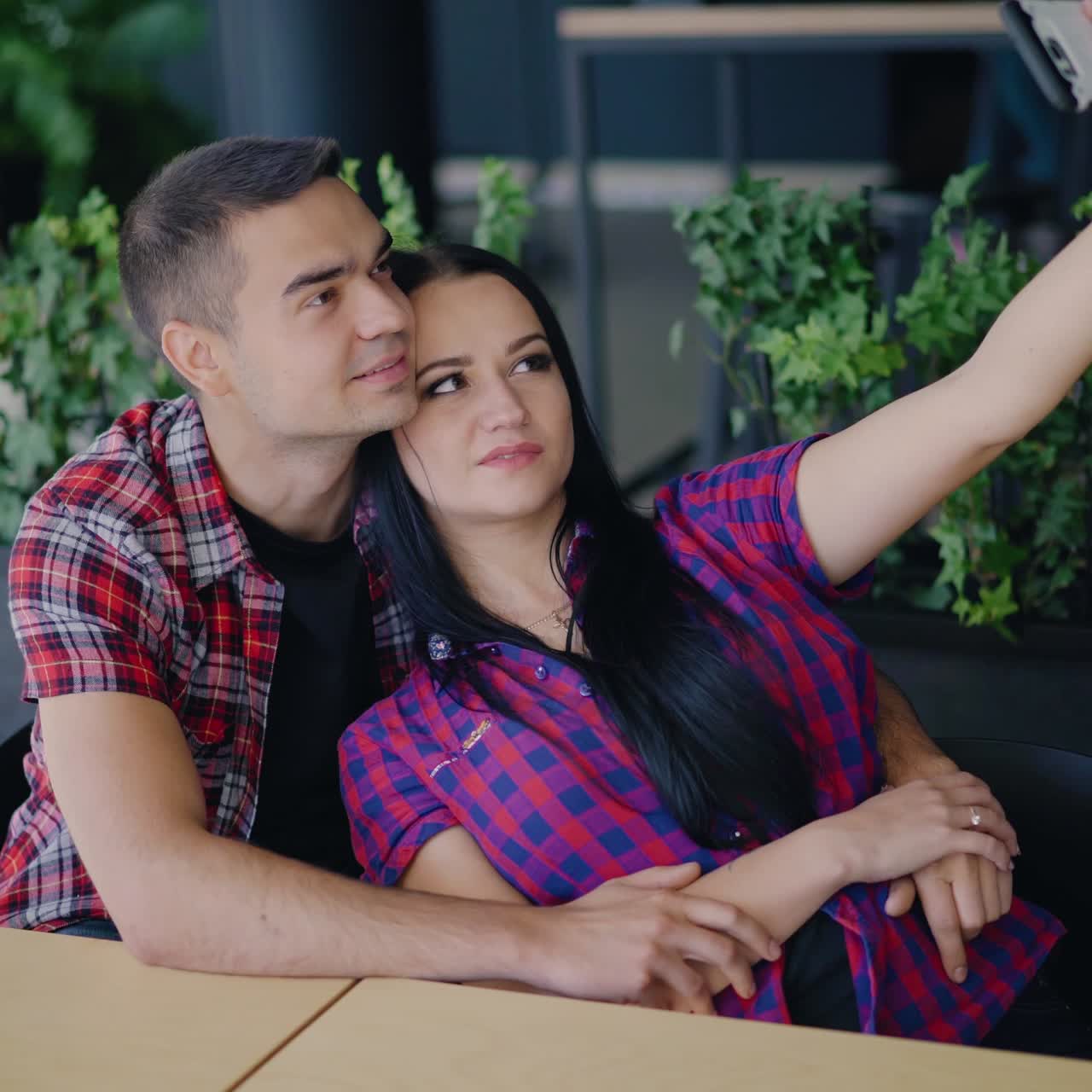a young couple are sitting at the table and making funny faces to each other in front of a phone in the restaurant