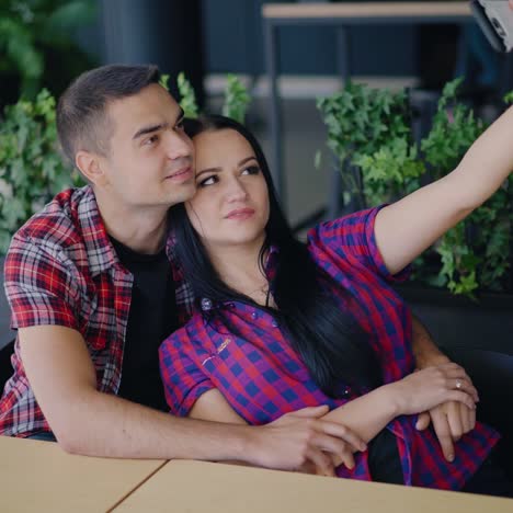a young couple are sitting at the table and making funny faces to each other in front of a phone in the restaurant