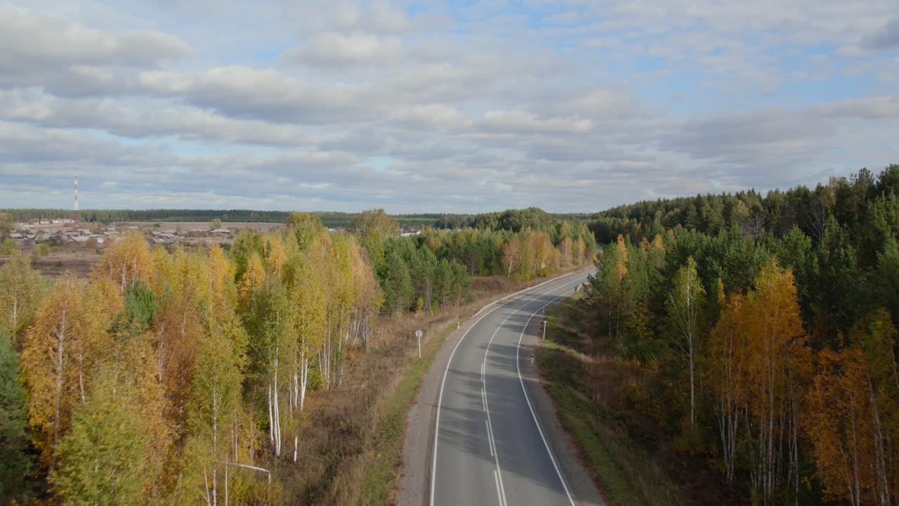 Záběry z dronu klikaté asfaltové silnice protínající smíšený březový a borový les v podzimních barvách pod zataženou oblohou, oblast Uralských hor, Rusko.
