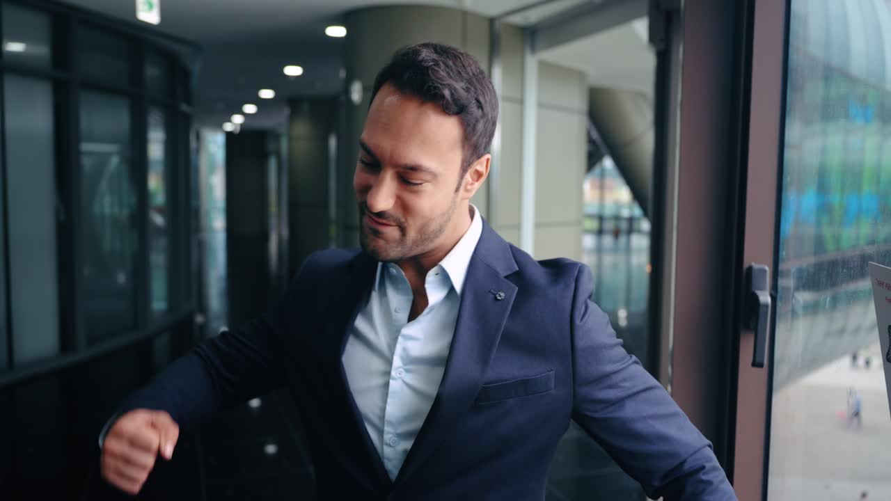 Happy and excited businessman in a suit celebrates a big success or good news with a joyful dance by the office window in slow motion