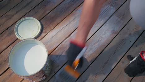 applying white decking to a wooden deck with a paint brush