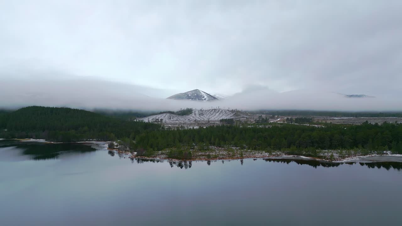 Heading across flat lake over forest towards a mist shrouded snow capped mountain