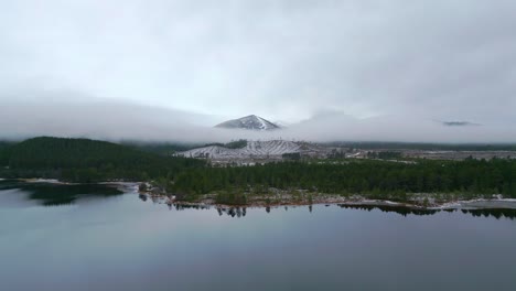 Heading-across-flat-lake-over-forest-towards-a-mist-shrouded-snow-capped-mountain