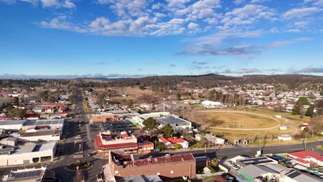 aerial footage glides above glen innes main street, revealing urban buildings, residential areas, and clear blue skies in bright daylight. smooth forward camera movement