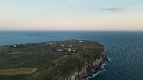 4k footage of the drone travelling towards portland bill's lighthouse, in dorset england, and going over it during a beautiful sunset.