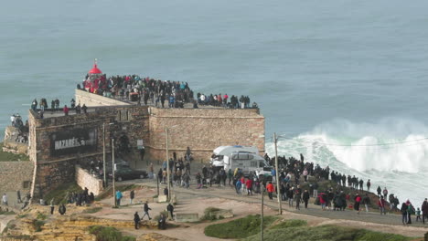 people enjoy watching intense waves on the nazaré lighthouse in portugal - slow motion shot