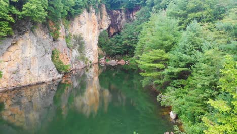 4K-Drone-Video-of-Beautiful-Mountain-Pond-Surrounded-by-Trees-and-Cliffs-at-Emerald-Village-near-Little-Switzerland,-NC-on-Summer-Day