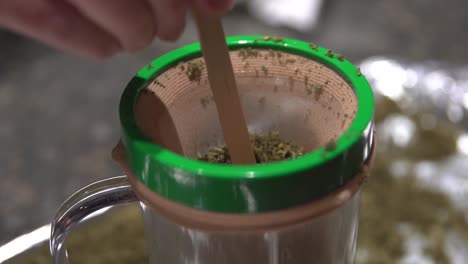 straining dry herb in a mason jar with muslin cloth and a wooden stick - salve oil making - close up slowmo