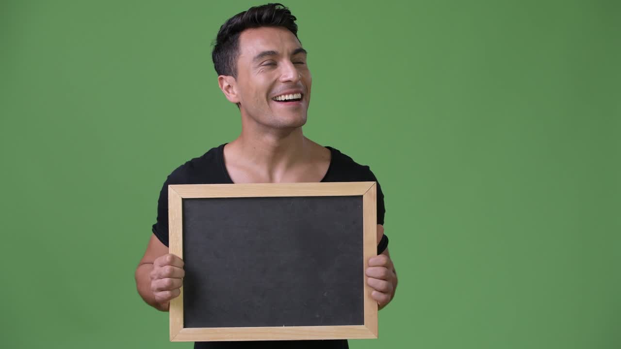 Young handsome Hispanic man against green background