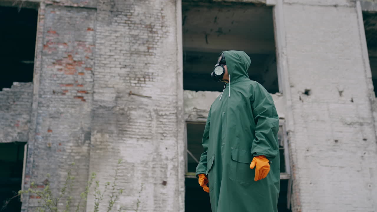 Person in a gas mask and safety suit outdoors. Man wearing respirator and protective uniform standing at post-apocalyptic place. Chemical attack.